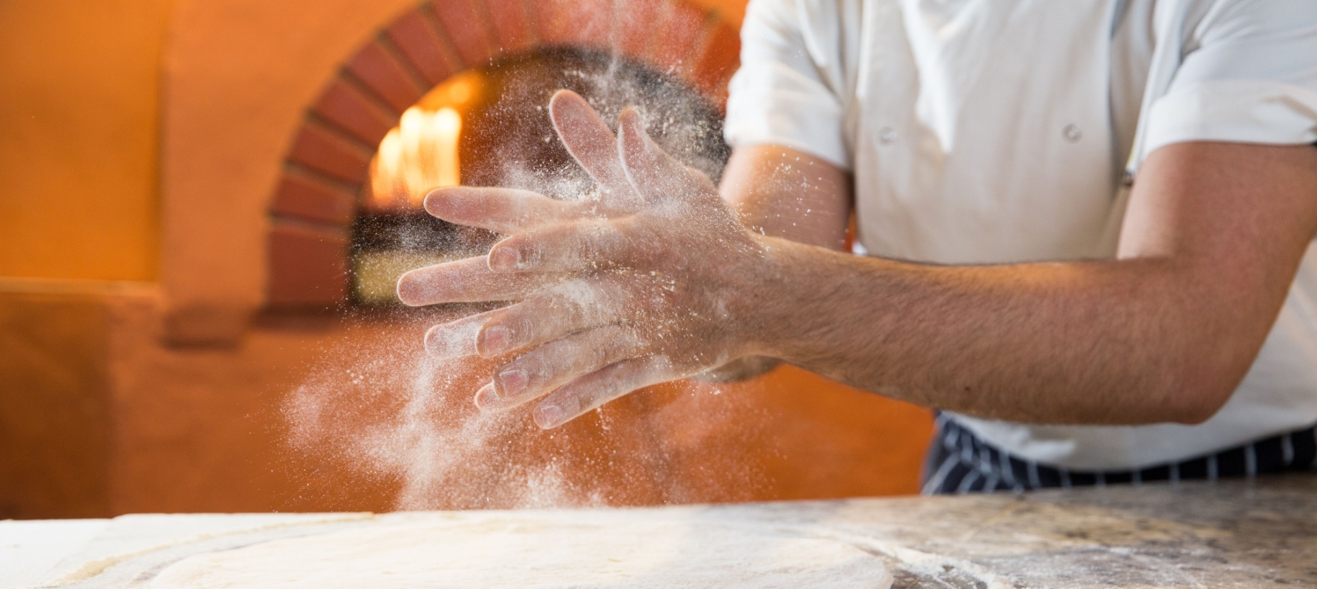 A chef claps his hand spreading flour into the air