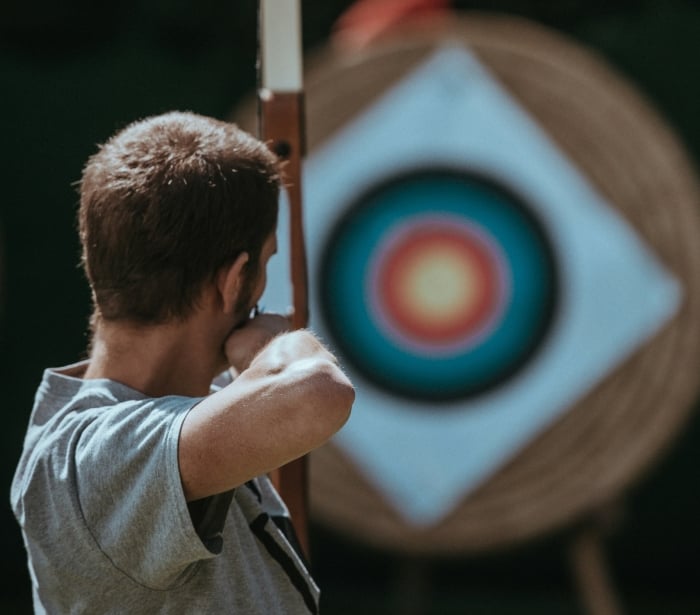 A focused man aiming at an arrow in front of a target.
