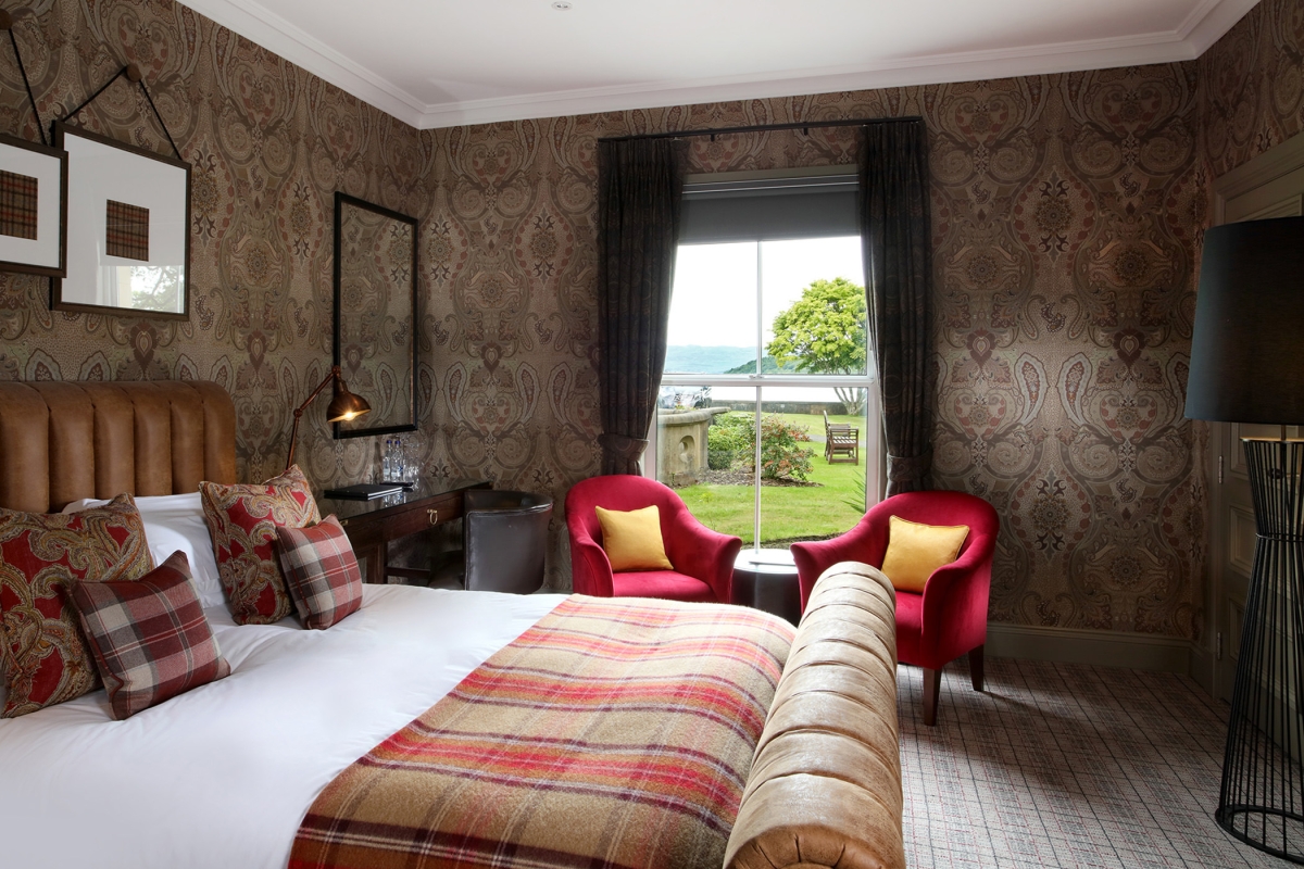 a bed with a night stand beside it and two red chairs in front of a window