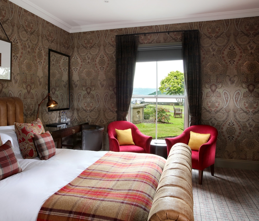 a bed with a night stand beside it and two red chairs in front of a window