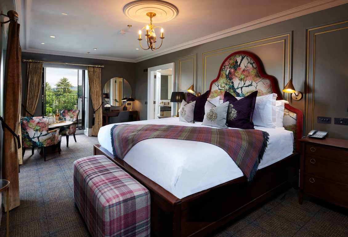 a large floral pattern bed with floral chairs surrounding a table and a door way to a patio