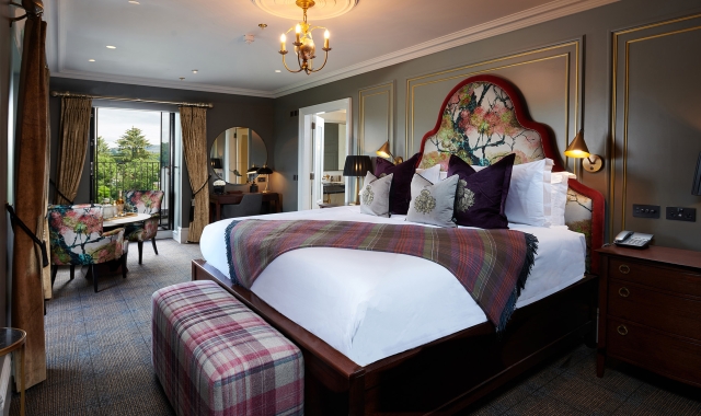 a large floral pattern bed with floral chairs surrounding a table and a door way to a patio