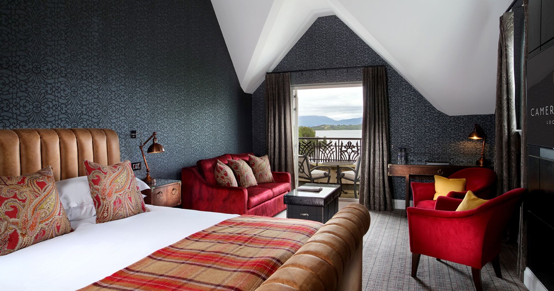 a bed sitting in a bed room with a red couch and two red chairs in front of a patio sitting area