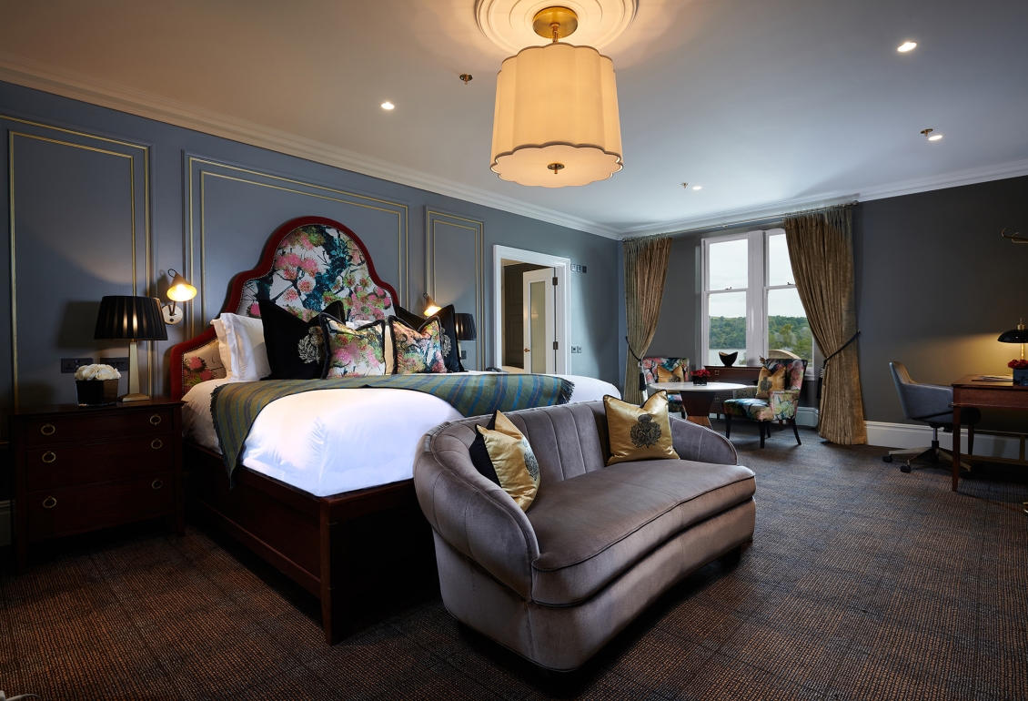 A luxurious suite at Cameron House featuring a bedroom with a bed, sofa, lamp, and table.