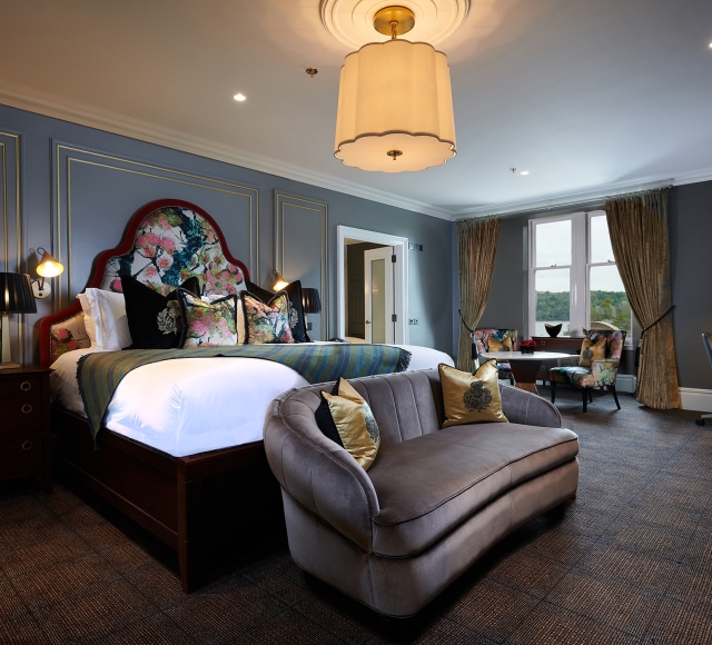 A luxurious suite at Cameron House featuring a bedroom with a bed, sofa, lamp, and table.