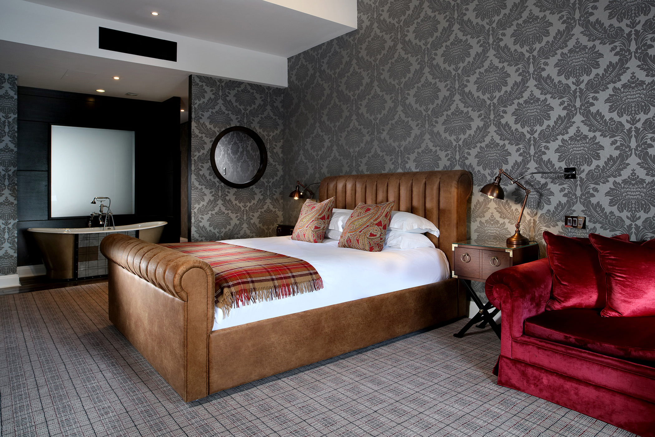 a bed sitting next to a red coach and a full sized tub on the other side of the room