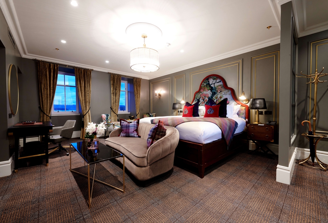 a bed room with a bright red trim around the head board and red pillows with couches and tables in front