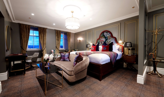 a bed room with a bright red trim around the head board and red pillows with couches and tables in front