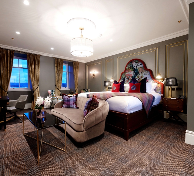 a bed room with a bright red trim around the head board and red pillows with couches and tables in front