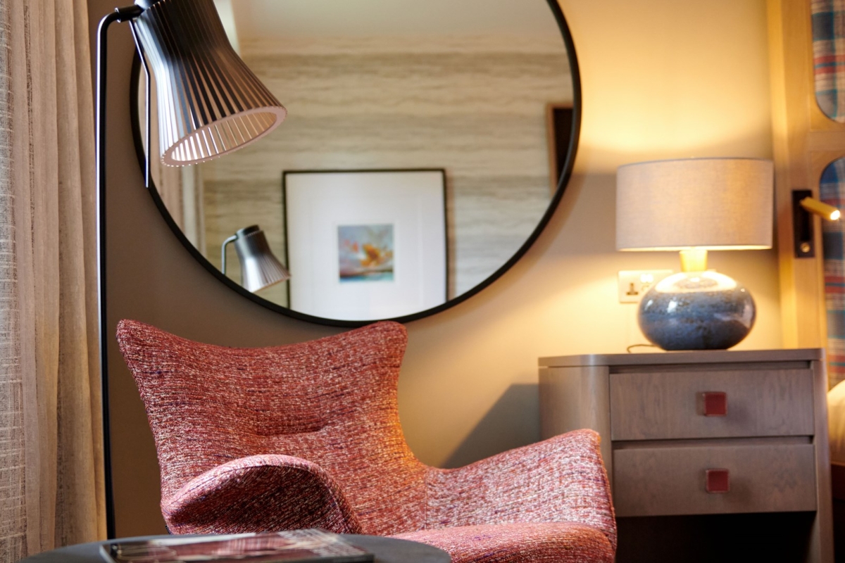 A comfortable hotel room chair with a large mirror above it.