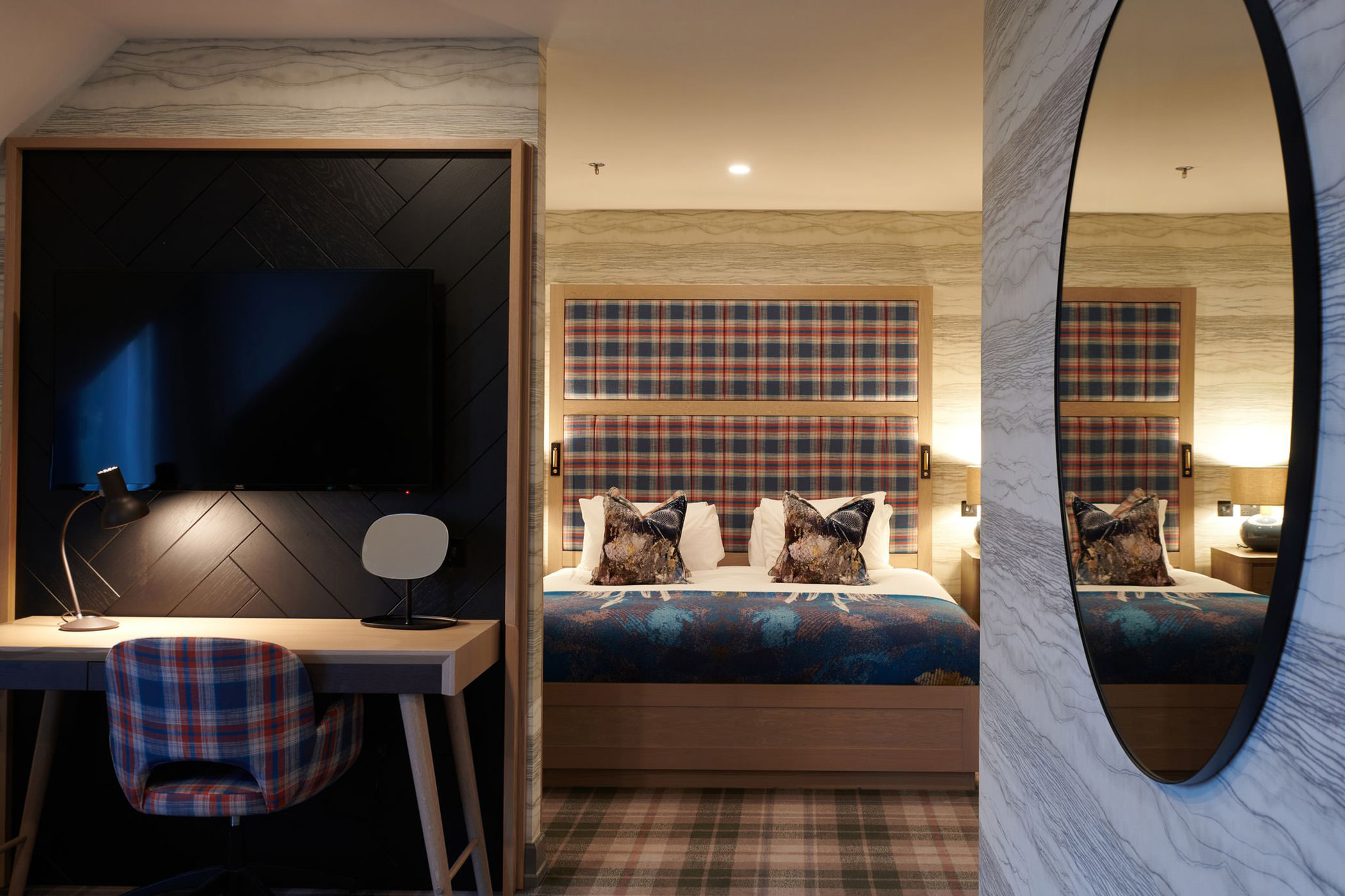 a working area in a bed room with a large bed and a large oval mirror hanging on a wall