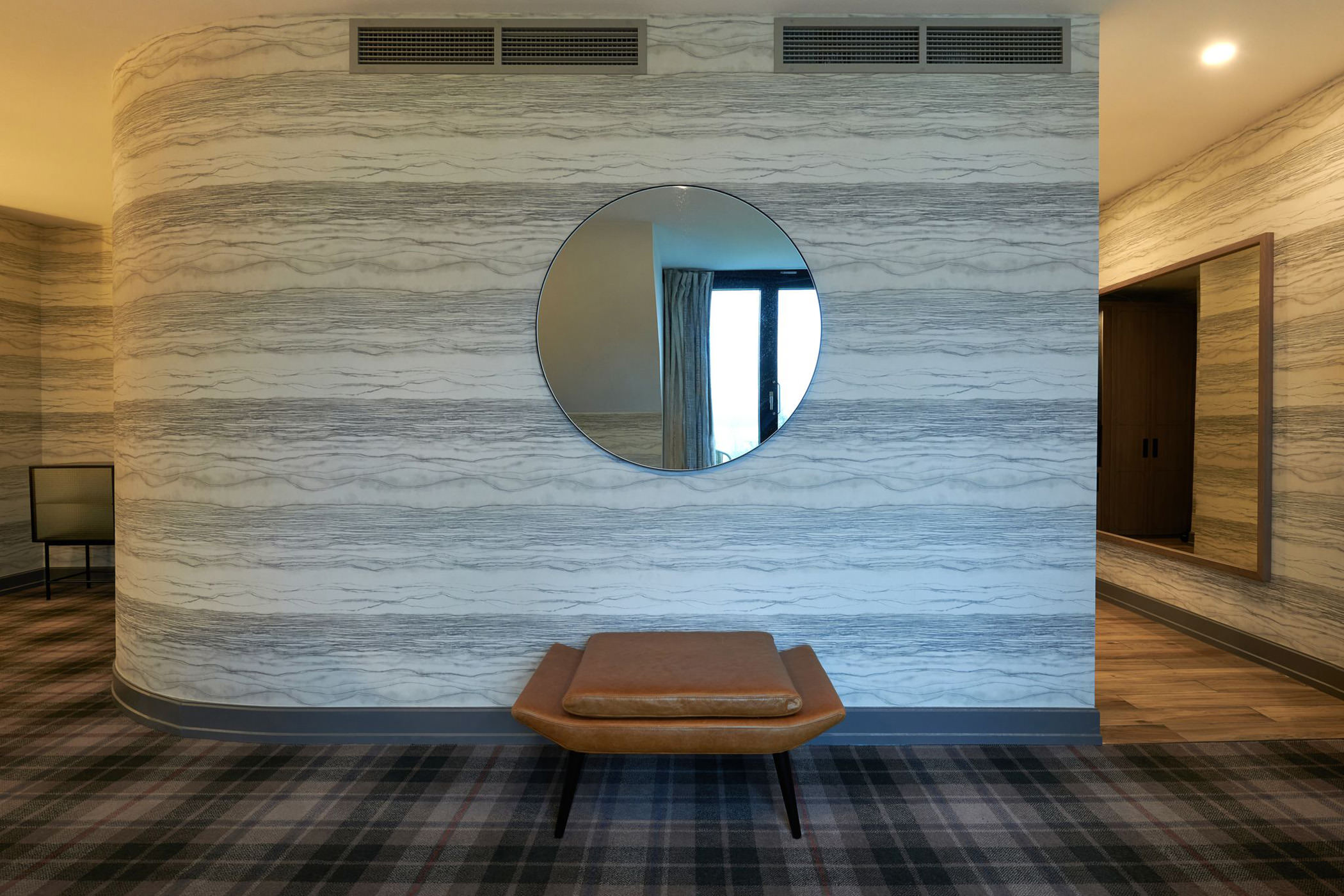 a small brown chair sitting in front of a round mirror hanging on a wall