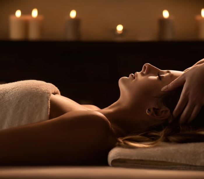 a woman laying on a table under a towel with candles in the background getting her forehead massaged