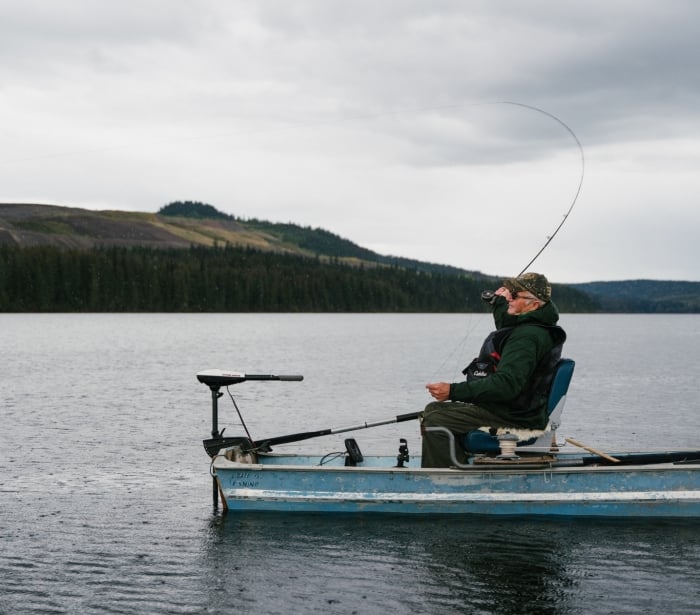 a man sitting on a old blue boat fishing in the middle of the water
