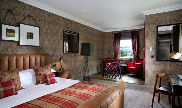 A cozy studio suite at Cameron House featuring a bed, chair, mirror, and wallpapered wall.