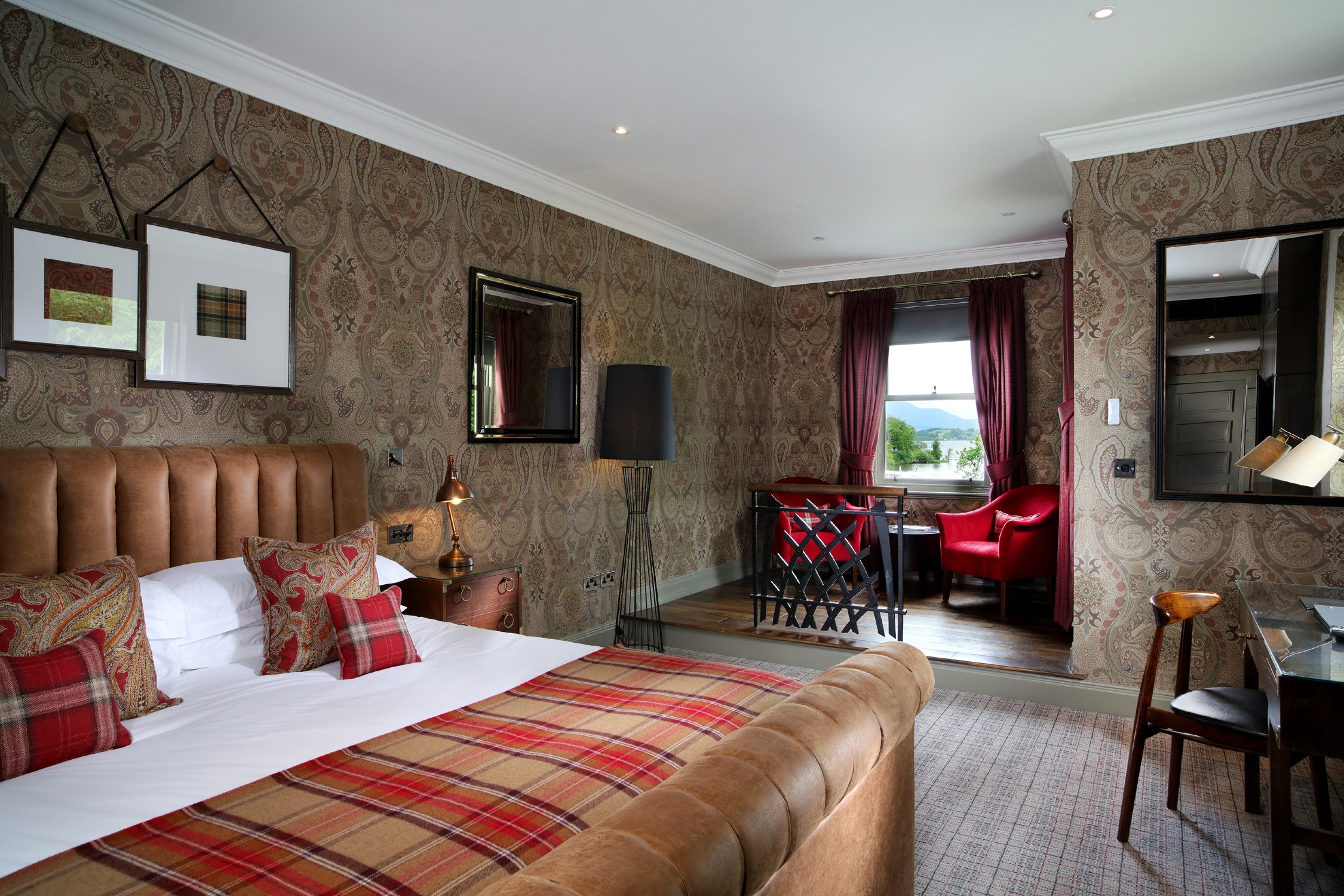 A cozy studio suite at Cameron House featuring a bed, chair, mirror, and wallpapered wall.