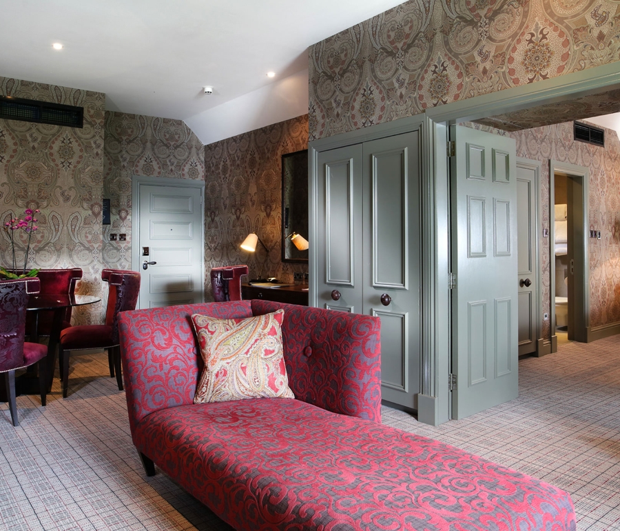 a floral themed lounge chair sitting in front of a open door way leading to a bed room