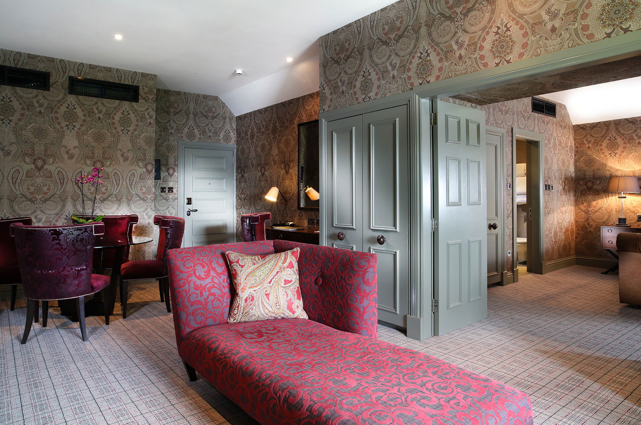 a floral themed lounge chair sitting in front of a open door way leading to a bed room