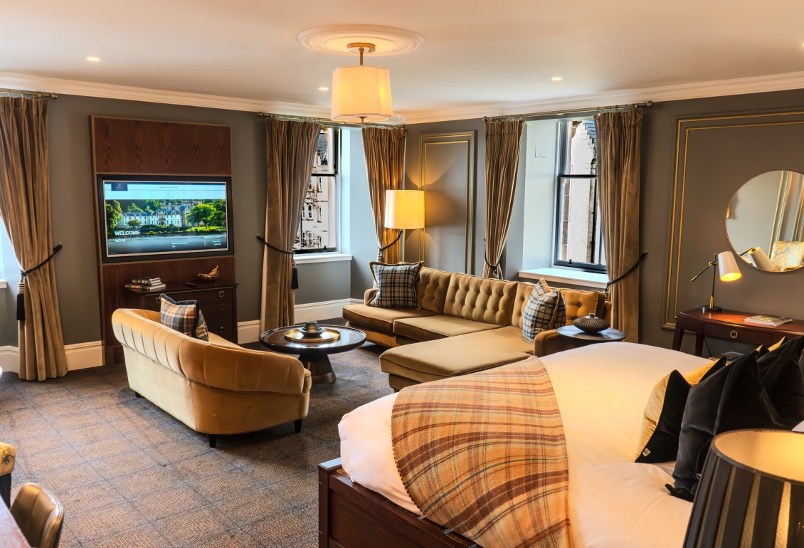 a living area in the loch view suite at Auld House with two sofas, a coffee table, flatscreen tv and large windows.