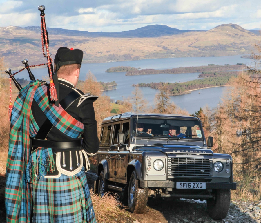 a male standing outside playing the bagpipes with a black suv in front of him
