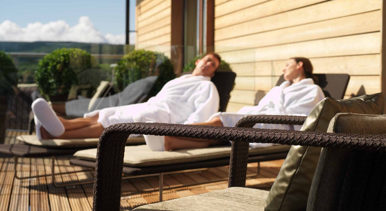 a male and female sitting outside in robes on lounge chairs enjoying the sun