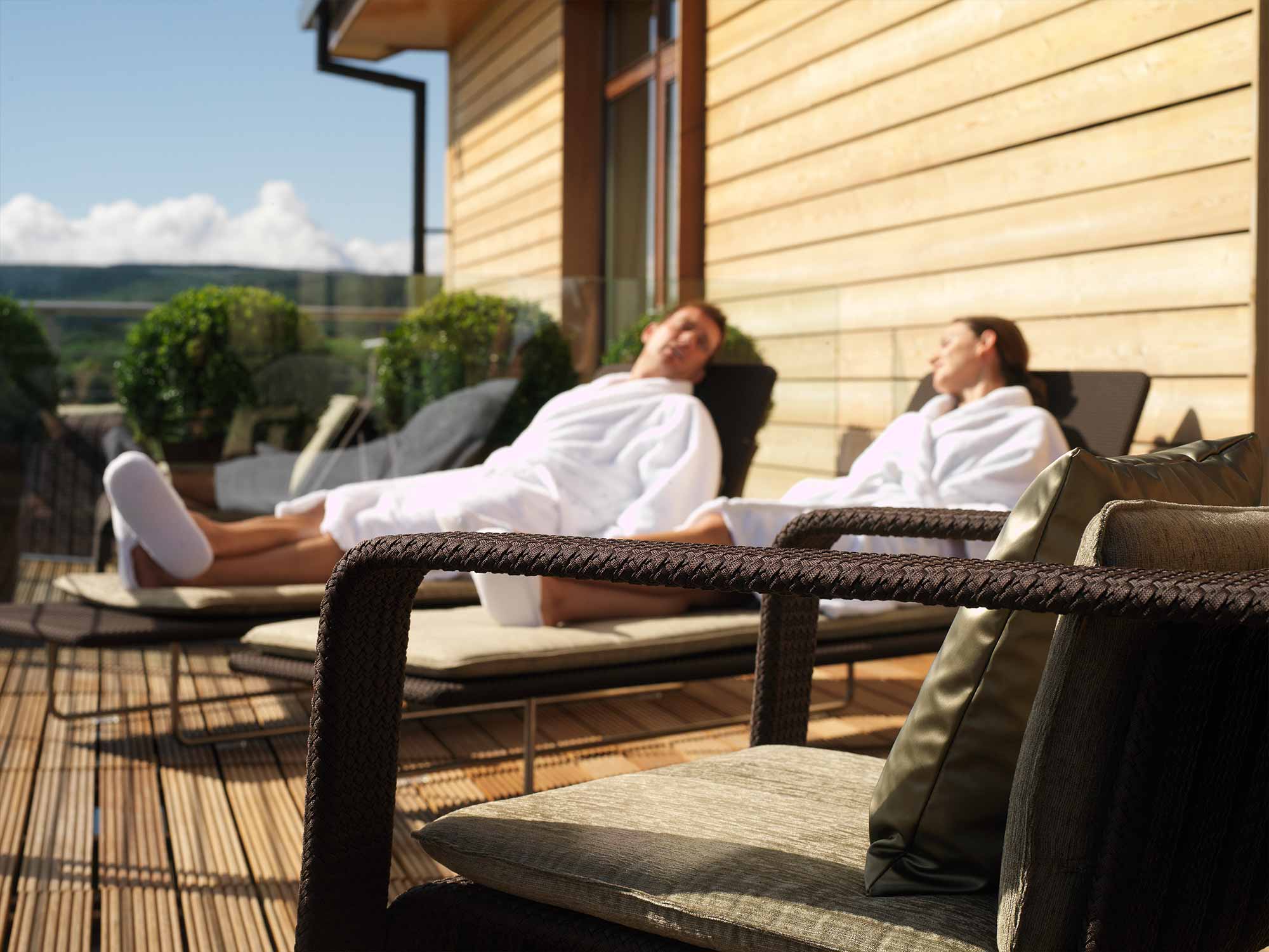 a male and female sitting outside in robes on lounge chairs enjoying the sun