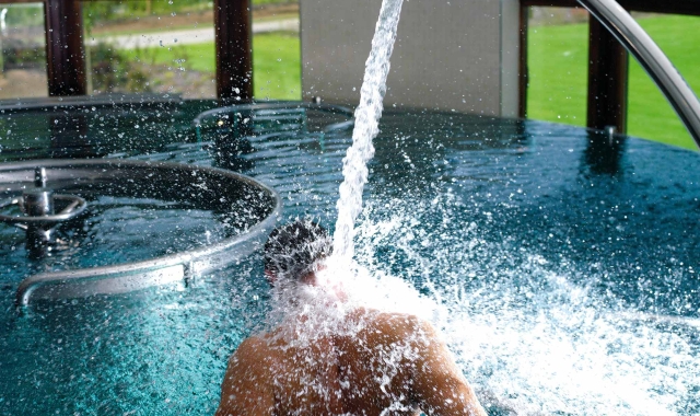 a person sitting in a pool with water flowing into the pool and great views of the outside in the background