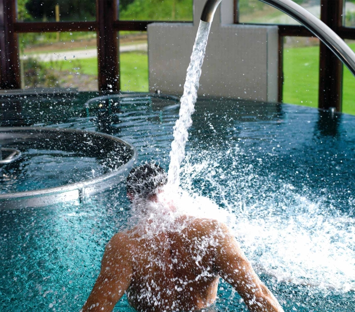 a person sitting in a pool with water flowing into the pool and great views of the outside in the background
