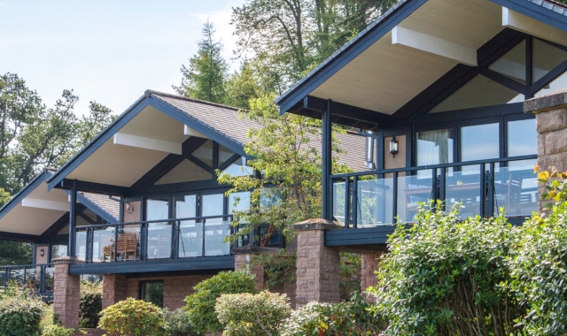 Exterior of the Cameron Lodges overlooking Loch Lomond, with lush green lawns and bushes in the foreground.