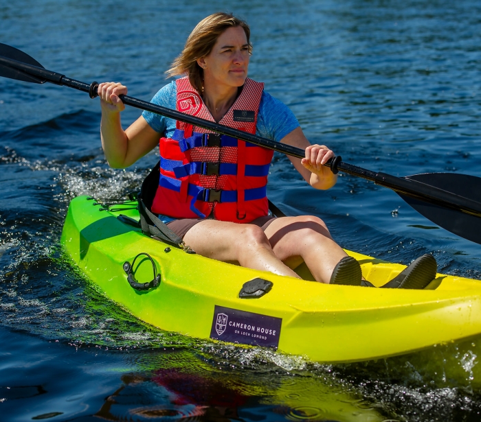 a woman sitting in a green and yellow canoe wearing a life jacket and holding a paddle in the lake