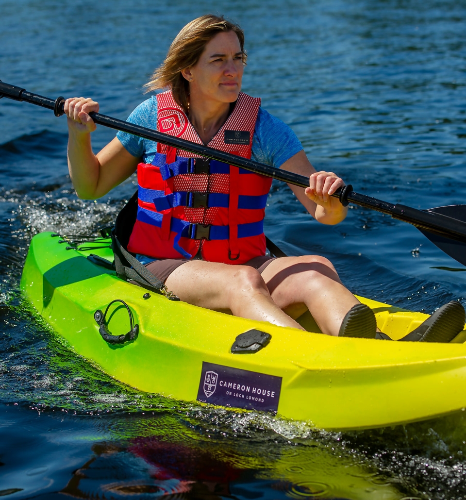 a woman sitting in a green and yellow canoe wearing a life jacket and holding a paddle in the lake