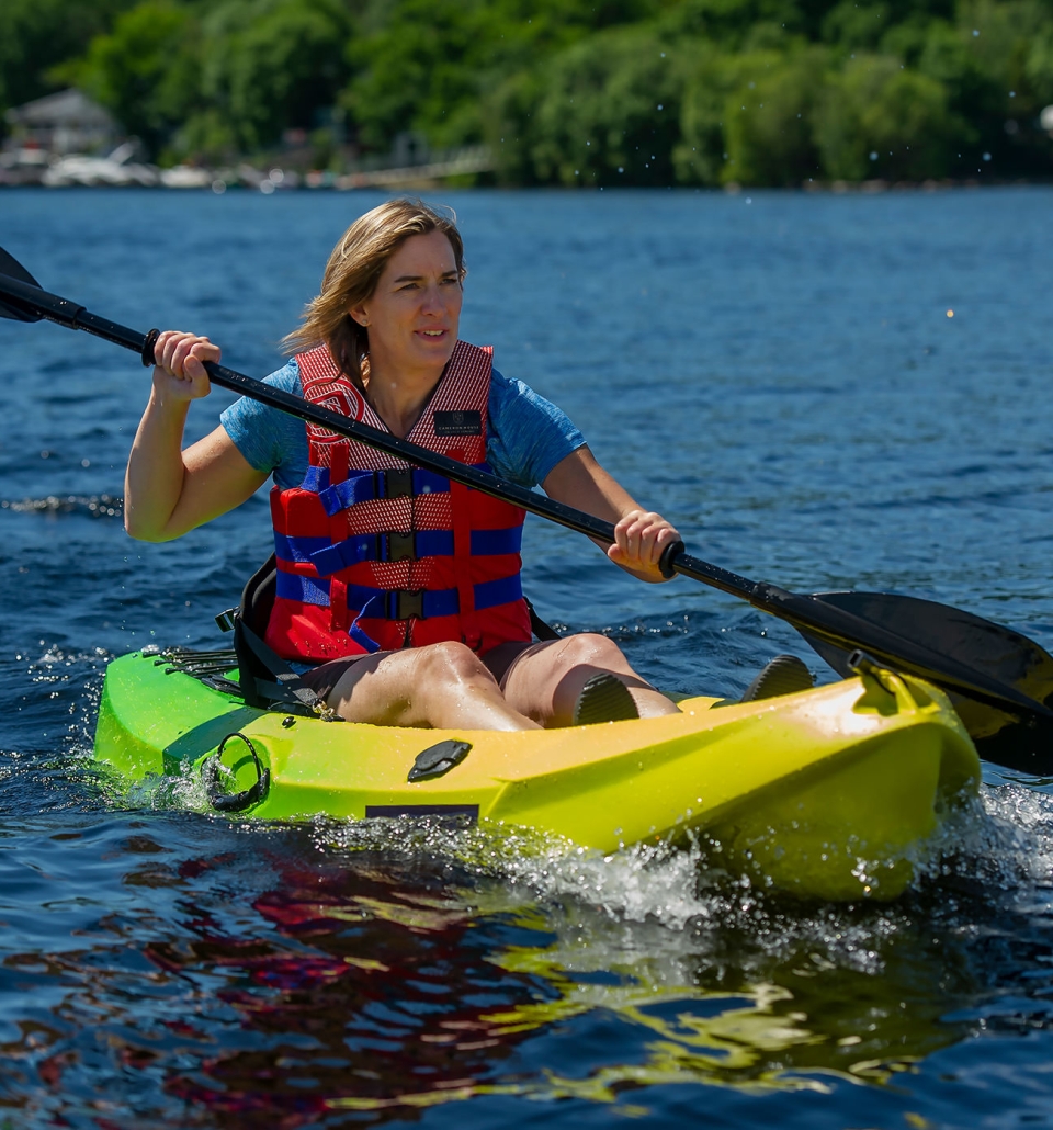 a woman sitting in a green and yellow canoe padding in the middle of a lake