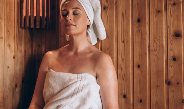 a woman wrapped in a towel and a towel on her head relaxing in a sauna