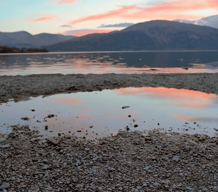 rock beach sitting on the edge of the water with mountains in the back ground