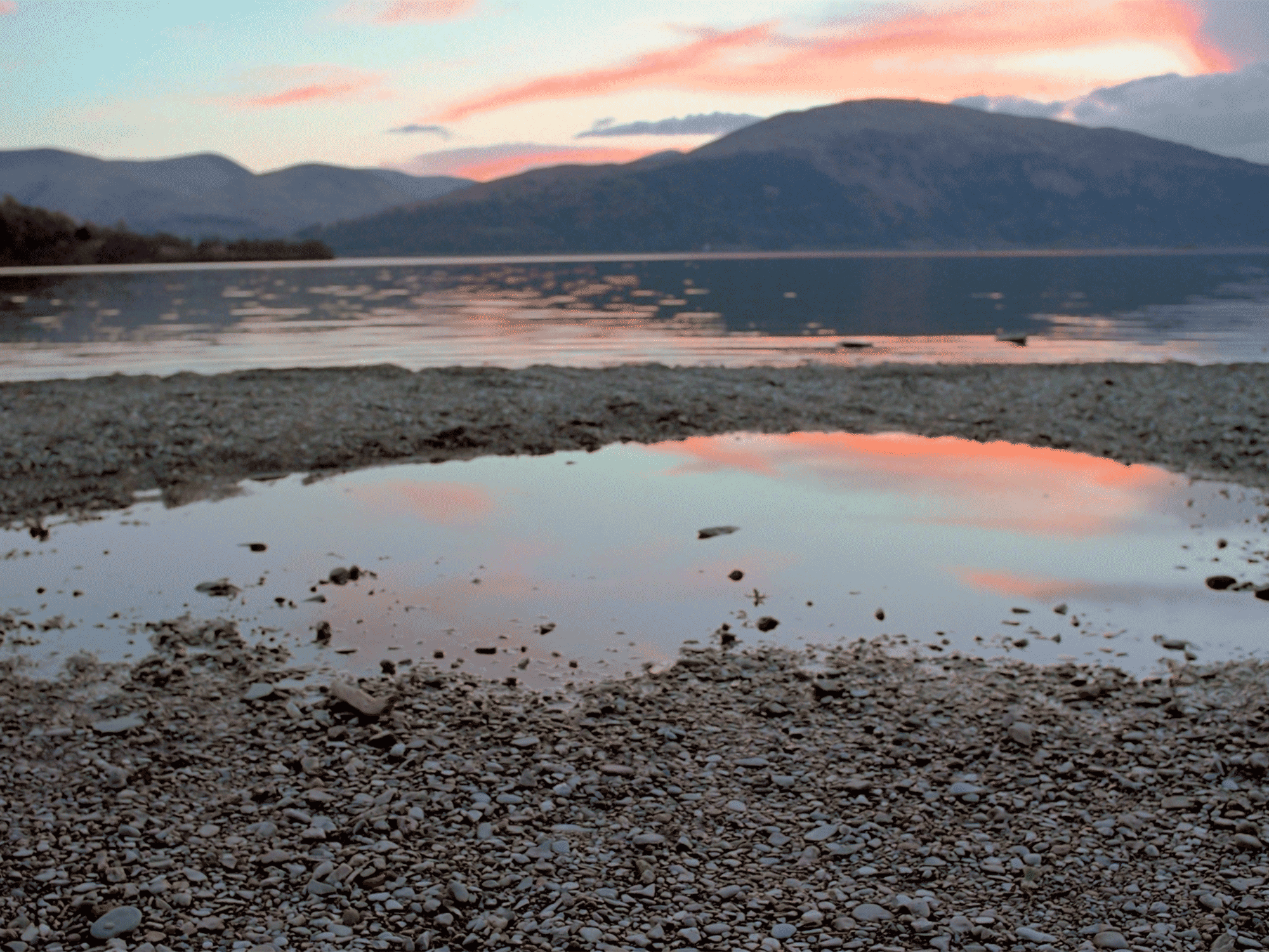 rock beach sitting on the edge of the water with mountains in the back ground
