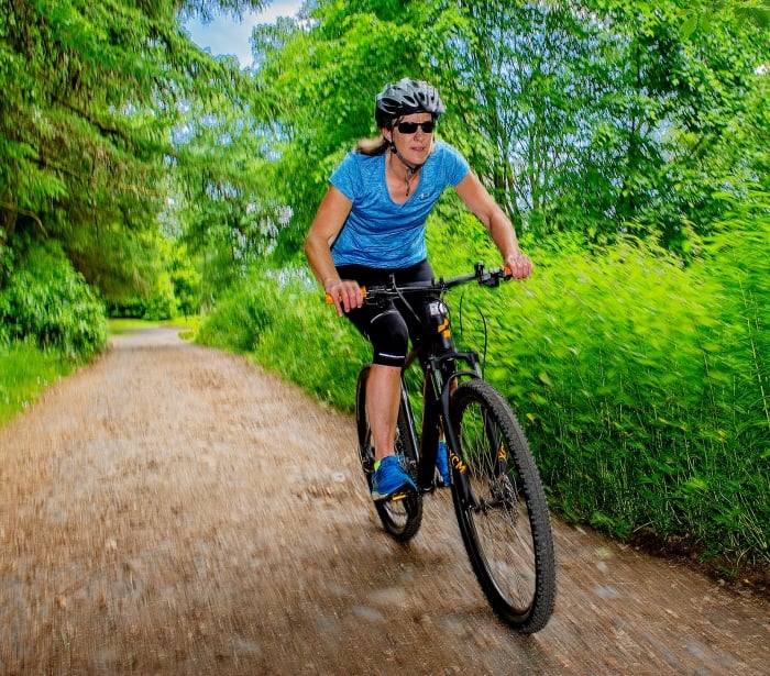 woman riding a bike outside down a dirt trail with green bushes around her