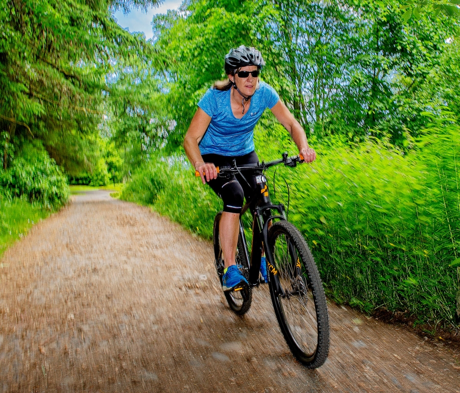 woman riding a bike outside down a dirt trail with green bushes around her