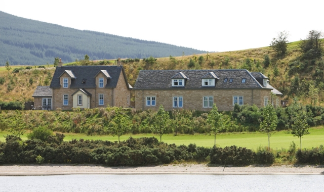 two buildings sitting lake side with hills sitting in the background