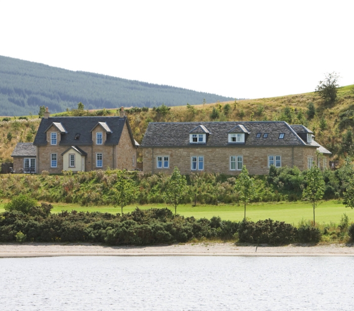 two buildings sitting lake side with hills sitting in the background