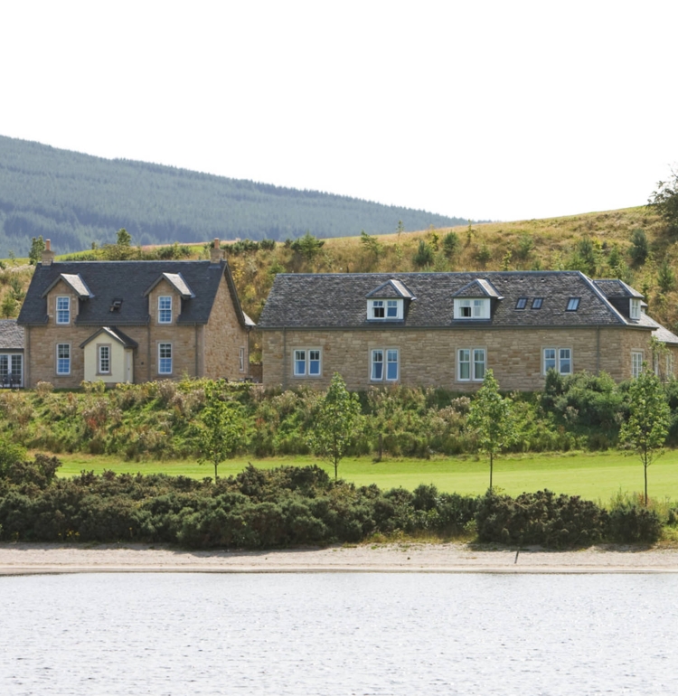 two cottages sitting lake side with hills sitting in the background