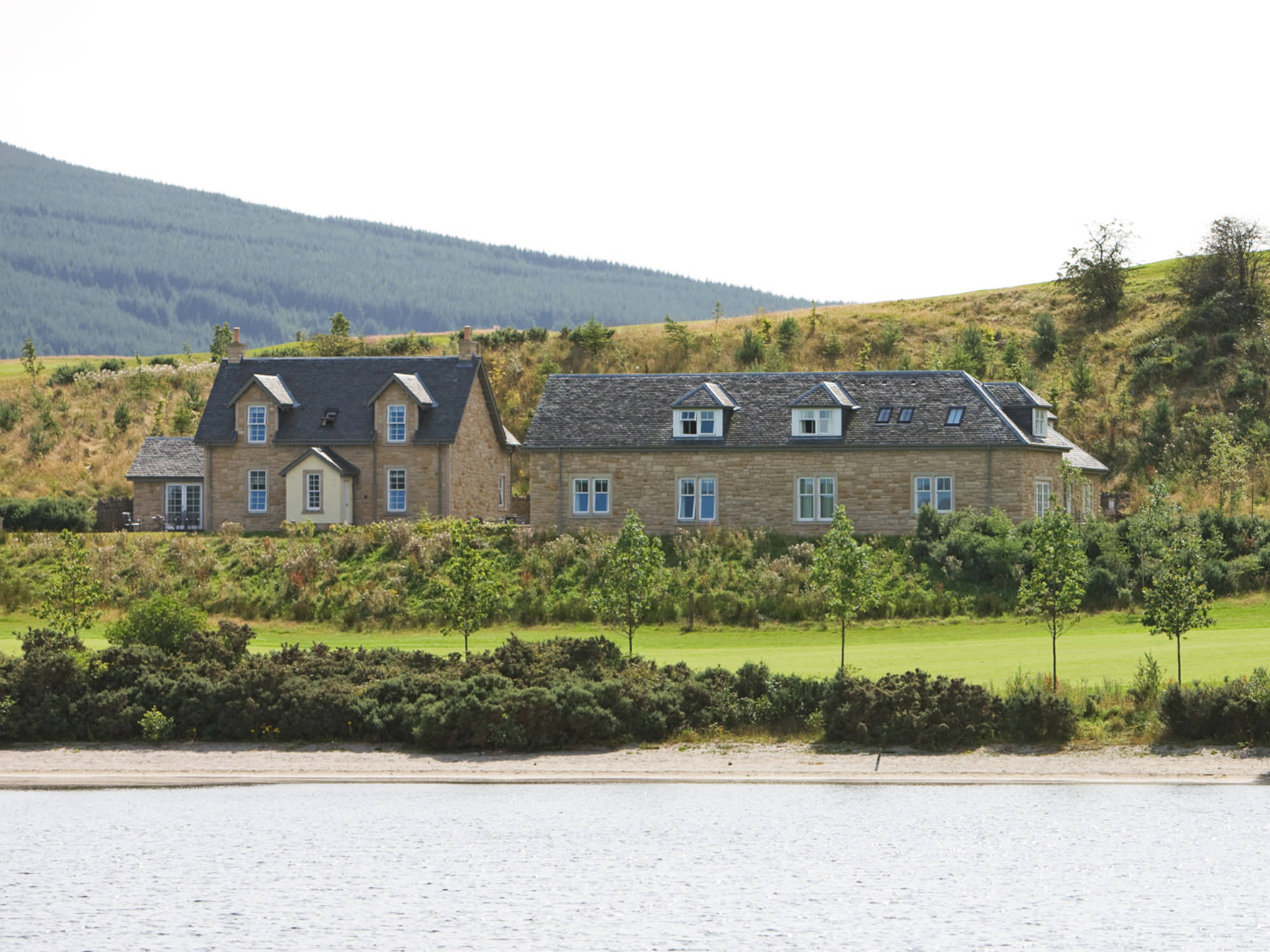 two buildings sitting lake side with hills sitting in the background