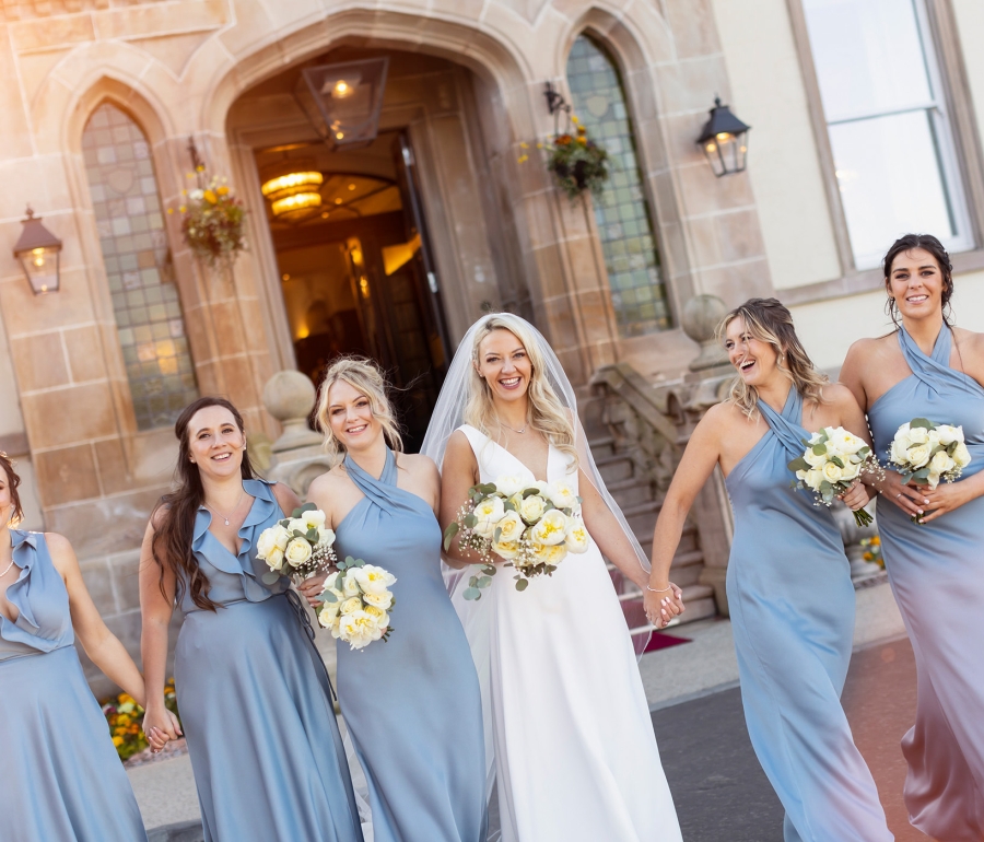 a groom and her bridesmaids standing outside in front of a building all holding bouquets