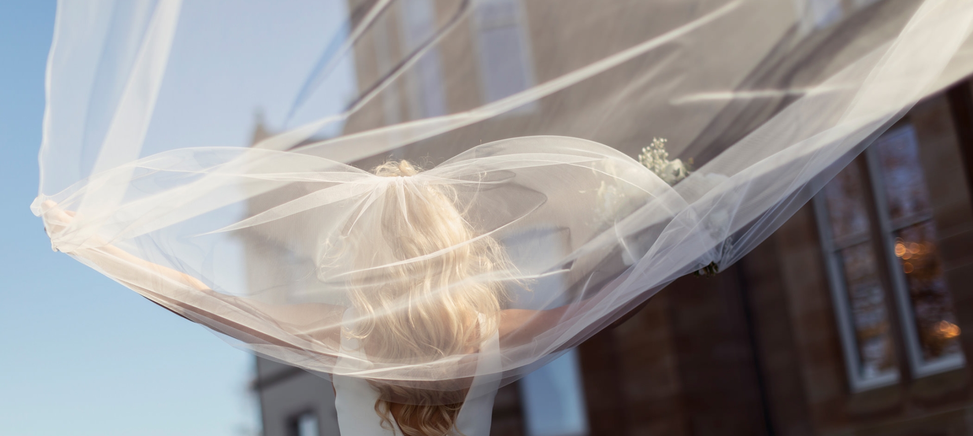 a bride standing outside on a sunny day throwing her vail backwards behind her