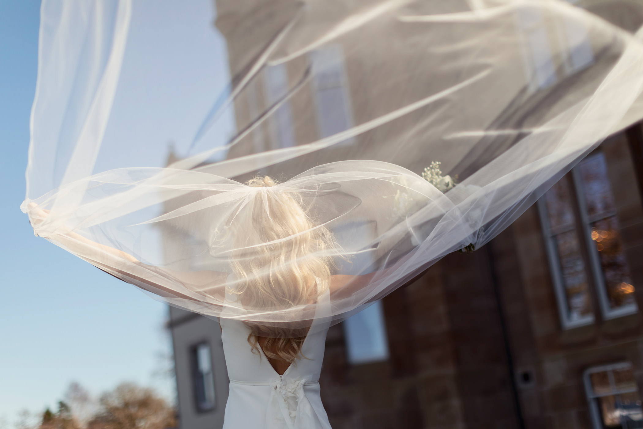 a bride standing outside on a sunny day throwing her vail backwards behind her