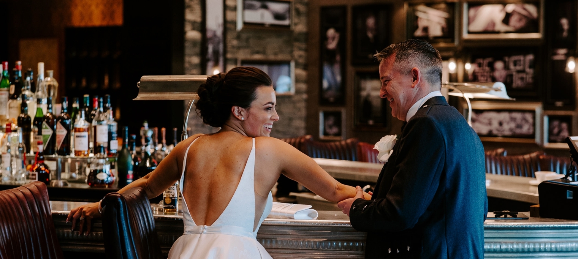 A bride and groom dressed up in their wedding clothing standing at a bar