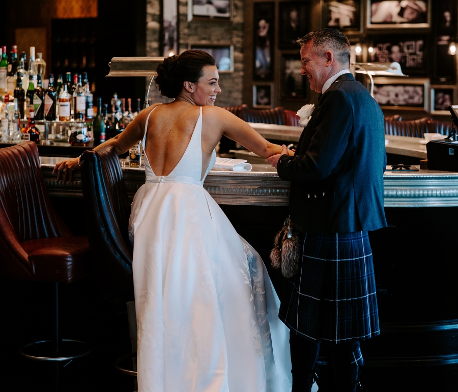 A bride and groom dressed up in their wedding clothing standing at a bar