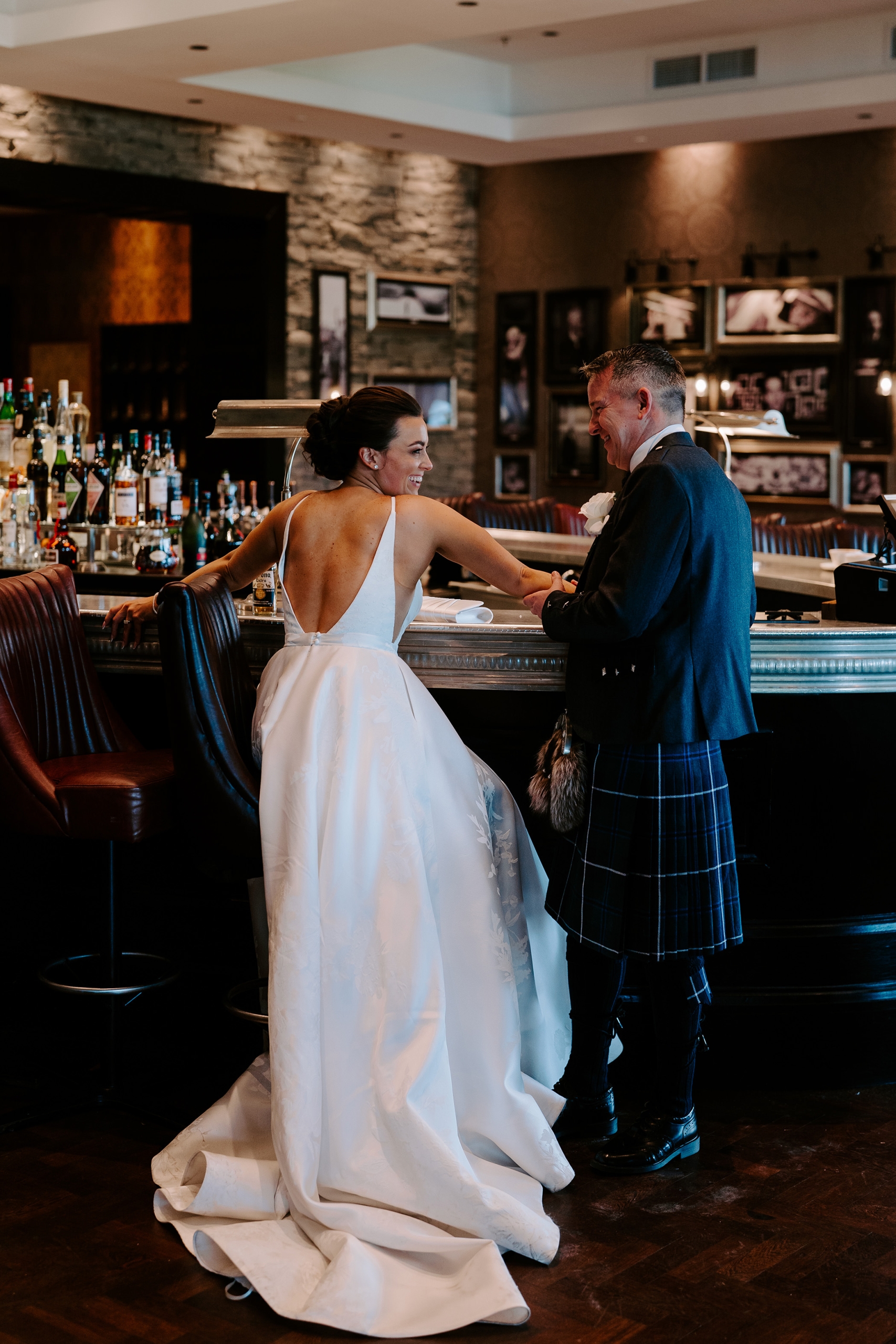A bride and groom dressed up in their wedding clothing standing at a bar