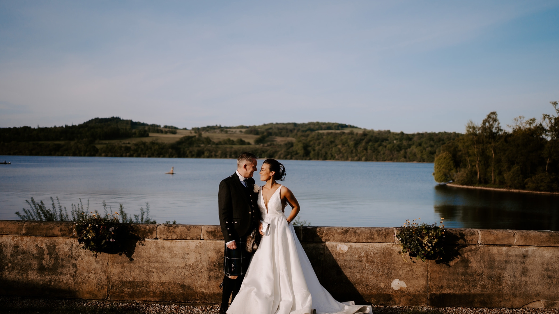 A bridge and groom gazing into each others eyes while standing in front of a massive lake