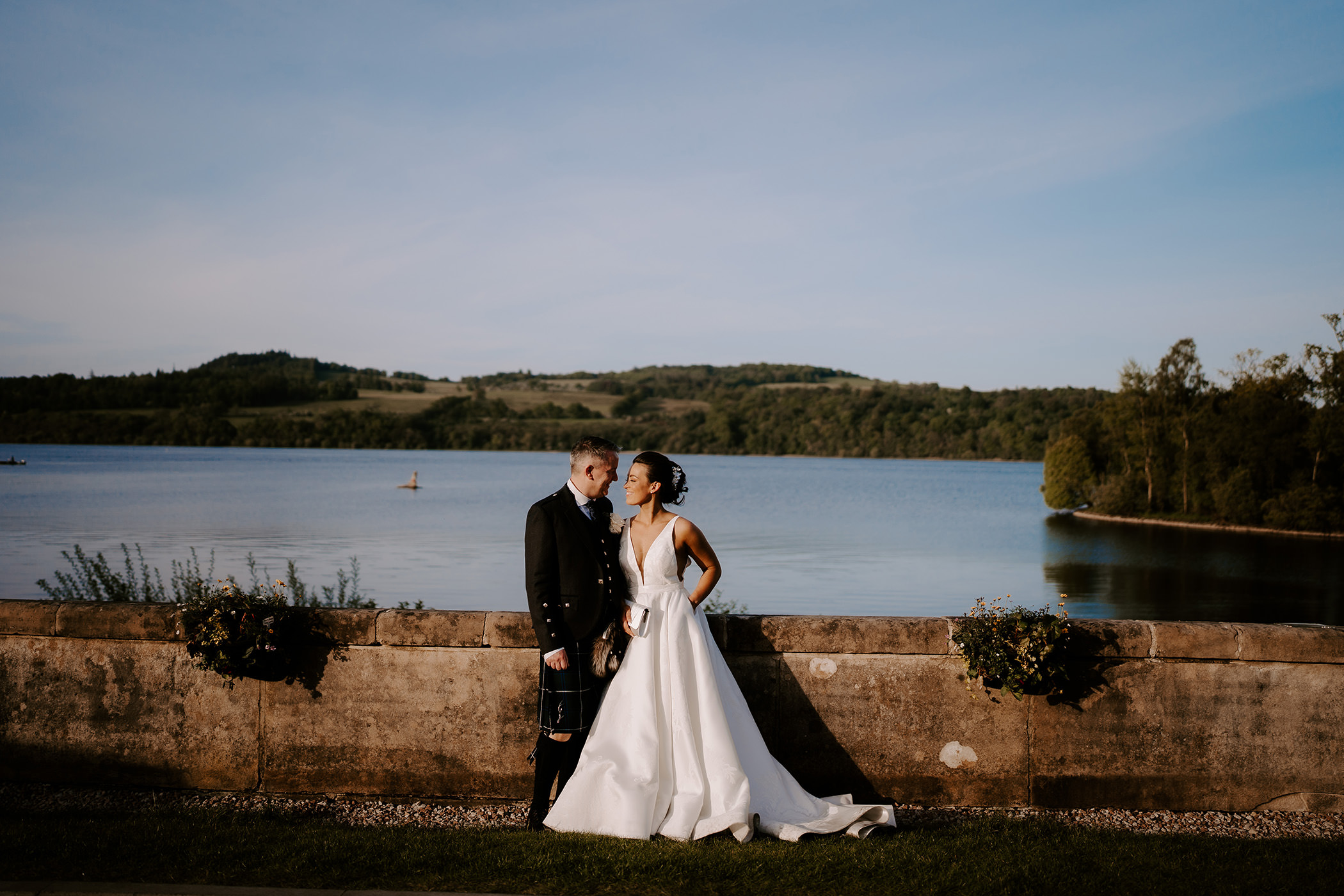 A bridge and groom gazing into each others eyes while standing in front of a massive lake