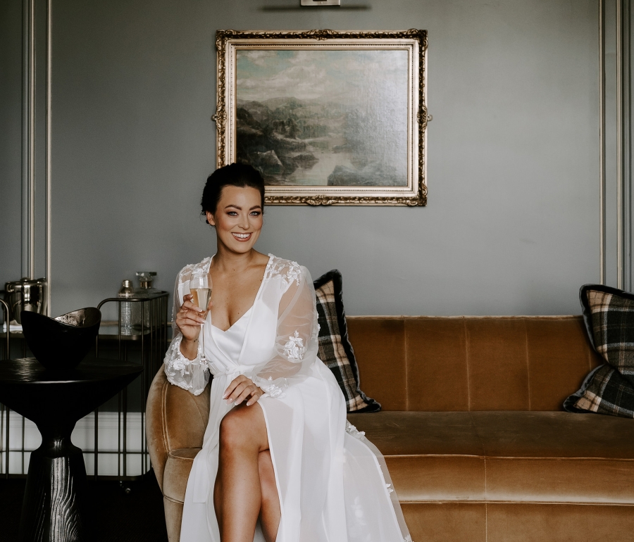 a bride sitting inside on a tan couch sipping holding a glass of water